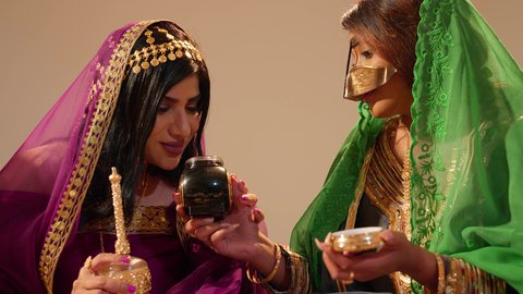 تعابير السعادة و السرور، العادات الشعبية في الأعراس الخليجية الاماراتية، تصوير مقرب لامراة عربيه خليجيه اماراتية ترتدي العباءة المطرزة  تمسك بعلبة بن تقدمها للعروس لتشم رائحتها، تحضيرات العروس قبل الزفاف