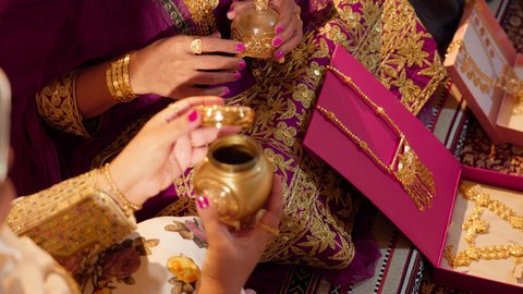 تعبير عن الفرح والمودة في المناسبات الخليجية، طقوس وعادات ما قبل الزفاف فى الامارات العربية، تصوير مقرب لام العريس ترتدي الزي المطرز تمسك بعلبة بن تقدمها للعروس لتشم رائحتها