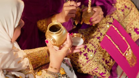 طقوس وعادات ما قبل الزفاف فى الامارات العربية، تصوير مقرب لام العريس ترتدي الزي المطرز تمسك بعلبة بن تقدمها للعروس لتشم رائحتها، تعبير عن الفرح والمودة في المناسبات الخليجية