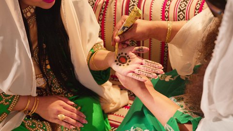 الاهتمام بالمظهر الخارجي والتجمل على الطريقة الشعبية، زخارف وفنون يدويه من مواد طبيعيه، عادات وتقاليد في المناسبات والأفراح السعيدة، تصوير مقرب ليد إمرأة عربية خليجية إماراتية ترتدي الزي التراثي و تقوم برسم و نقش الحنة على يد شابة، مهن وأزياء تقليدية شعبية نسائية