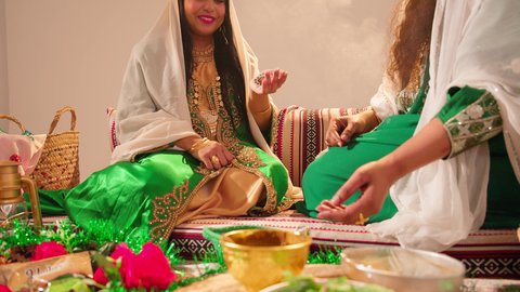 تعابير السعادة والسرور، أزياء تقليدية شعبية نسائية، فنون ونقوش وزخارف يدويه من مواد طبيعيه، التجمل والتزيين في يوم الزفاف، عادات وتقاليد في المناسبات والأفراح السعيدة، إمرأة عربية خليجية إماراتية تقوم بالرسم والنقش على يد شابة سعودية باستخدام الحناء الحمراء