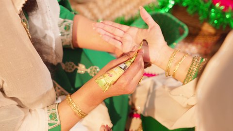 فنون ونقوش وزخارف يدويه من مواد طبيعيه، التجمل والتزيين والاهتمام بالمظهر الخارجي، عادات وتقاليد في المناسبات والأفراح السعيدة، صورة مقربة ليد إمرأة عربية خليجية إماراتية تقوم بالرسم والنقش على يد فتاة باستخدام الحناء الحمراء، مهنة تقليدية شعبية نسائية