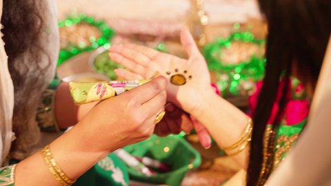 الاهتمام بالمظهر الخارجي والتجمل على الطريقة الشعبية، زخارف وفنون يدويه من مواد طبيعيه، عادات وتقاليد في المناسبات والأفراح السعيدة، تصوير مقرب ليد إمرأة عربية خليجية إماراتية ترتدي الزي التراثي و تقوم برسم و نقش الحنة على يد شابة، مهن وأزياء تقليدية شعبية نسائية