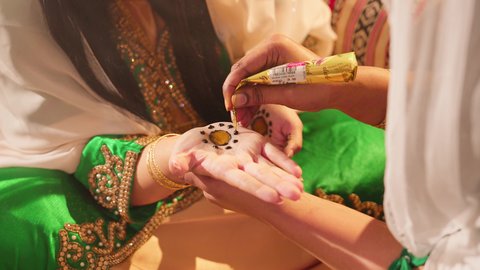 فنون ونقوش وزخارف يدويه من مواد طبيعيه، التجمل والتزيين والاهتمام بالمظهر الخارجي، عادات وتقاليد في المناسبات والأفراح السعيدة، صورة مقربة ليد إمرأة عربية خليجية إماراتية تقوم بالرسم والنقش على يد فتاة باستخدام الحناء الحمراء، مهنة تقليدية شعبية نسائية