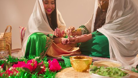 ايماءات السعادة والسرور، أزياء تقليدية شعبية نسائية، فنون ونقوش وزخارف يدويه من مواد طبيعيه، التجمل والتزيين في يوم الزفاف، عادات وتقاليد في المناسبات والأفراح السعيدة، إمرأة عربية خليجية إماراتية تقوم بالرسم والنقش على يد شابة سعودية باستخدام الحناء الحمراء