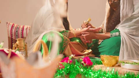 Gestures of happiness and joy, traditional popular women's clothing, arts, designs, and handmade decorations from natural materials, beautification and adornment on the wedding day, customs and traditions in happy occasions and celebrations, an Emirati Gulf Arab woman is drawing and engraving on the hand of a young Saudi woman using red henna.