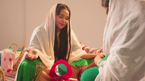 العناية والاهتمام بالأناقة والجمال، مفهوم التزين والاطلالة المتألقة، ايماءات السعادة والفرح، الاحتفال بليلة العمر، منتجات ومساحيق التجميل, مناسبات وأفراح واحتفالات سعيدة، سيدة عربية خليجية اماراتية تقوم بوضع المكياج للعروسة، ارتداء الازياء التقليدية