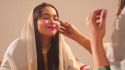 مفهوم التزين والاطلالة المتألقة، ايماءات السعادة والفرح، الاحتفال بليلة العمر، منتجات ومساحيق التجميل, مناسبات وأفراح واحتفالات سعيدة، العناية والاهتمام بالأناقة والجمال، سيدة عربية خليجية اماراتية تقوم بوضع المكياج للعروسة، ارتداء الازياء التقليدية