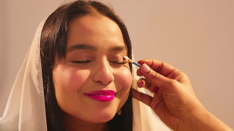 العناية والاهتمام بالأناقة والجمال، مفهوم التزين والاطلالة المتألقة، ايماءات السعادة والفرح، الاحتفال بليلة العمر، منتجات ومساحيق التجميل, مناسبات وأفراح واحتفالات سعيدة، سيدة عربية خليجية اماراتية تقوم بوضع المكياج للعروسة، ارتداء الازياء التقليدية