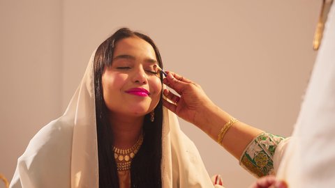 مفهوم التزين والاطلالة المتألقة، ايماءات السعادة والفرح، الاحتفال بليلة العمر، منتجات ومساحيق التجميل, مناسبات وأفراح واحتفالات سعيدة، العناية والاهتمام بالأناقة والجمال، سيدة عربية خليجية اماراتية تقوم بوضع المكياج للعروسة، ارتداء الازياء التقليدية