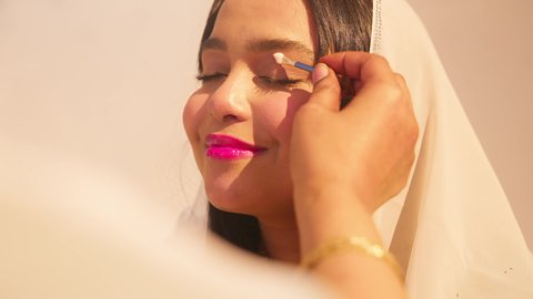 العناية والاهتمام بالأناقة والجمال، مفهوم التزين والاطلالة المتألقة، ايماءات السعادة والفرح، الاحتفال بليلة العمر، منتجات ومساحيق التجميل, مناسبات وأفراح واحتفالات سعيدة، سيدة عربية خليجية اماراتية تقوم بوضع المكياج للعروسة، ارتداء الازياء التقليدية