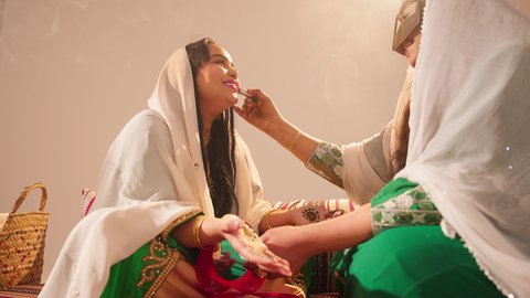 الاحتفال بليلة العمر، منتجات ومساحيق التجميل, مناسبات وأفراح واحتفالات سعيدة، العناية والاهتمام بالأناقة والجمال، مفهوم التزين والاطلالة المتألقة، سيدة عربية خليجية اماراتية تقوم بوضع أحمر الشفاه للعروسة، إيماءات السعادة والفرح