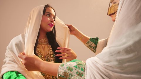 الاهتمام بالأناقة والمظهر الخارجي، مفهوم التزين والاطلالة المتألقة، سيدة عربية خليجية اماراتية ترتدي الزي التقليدي والبرقع تقوم بوضع الطرحة للعروسة، إيماءات السعادة والفرح ، الاحتفال بليلة العمر، مناسبات وأفراح واحتفالات سعيدة