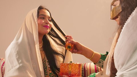 مفهوم الأناقة والاهتمام بالمظهر الخارجي، عطور ذات روائح فاخرة وفريدة، تصوير مقرب لسيدة عربية اماراتية خليجية تحمل زجاجة عطرية تقوم بوضع العطر لعروس ترتدي الزي التراثي، مراسم الأعراس والاحتفالات في الامارات، الفرح و السرورفي يوم الزواج