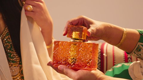 وضع الطيب على المعصم ، عطور ذات روائح فاخرة وفريدة، مفهوم الأناقة والاهتمام بالمظهر الخارجي، تصوير مقرب لسيدة عربية اماراتية خليجية تحمل زجاجة عطرية تقوم بوضع العطر لعروس ترتدي الزي التراثي، مراسم الأعراس والاحتفالات في الامارات، الفرح و السرورفي يوم الزواج