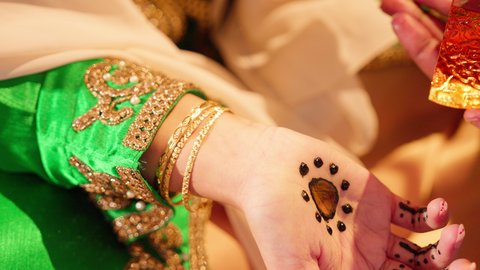 وضع الطيب على المعصم ، عطور ذات روائح فاخرة وفريدة، مفهوم الأناقة والاهتمام بالمظهر الخارجي، تصوير مقرب لسيدة عربية اماراتية خليجية تحمل زجاجة عطرية تقوم بوضع العطر لعروس ترتدي الزي التراثي، مراسم الأعراس والاحتفالات في الامارات، الفرح و السرورفي يوم الزواج