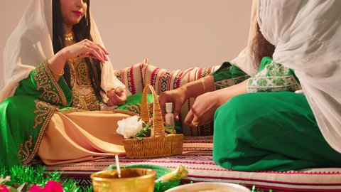 الاستعداد من اجل ليلة العمر، ازياء تقليدية شعبية نسائية، عادات وتقاليد في المناسبات والأفراح السعيدة، الاهتمام بالأناقة والمظهر الخارجي, امرأة عربية خليجية إماراتية محجبة ترتدي الزي الشعبي تقوم بوضع طلاء الأظافر للعروسة, شابة سعودية تقوم بالتزين والتجمل في يوم زفافها