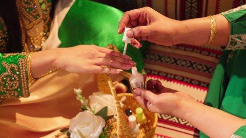 الاهتمام بالأناقة والمظهر الخارجي, الاستعداد من اجل ليلة العمر، ازياء تقليدية شعبية نسائية، عادات وتقاليد في المناسبات والأفراح السعيدة، امرأة عربية خليجية إماراتية محجبة ترتدي الزي الشعبي تقوم بوضع طلاء الأظافر للعروسة, شابة سعودية تقوم بالتزين والتجمل في يوم زفافها