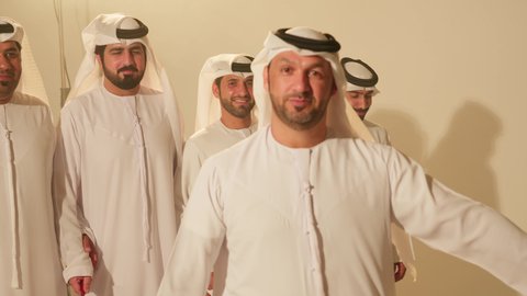 Gestures of joy and pride, a traditional celebration and national occasion, a heritage folklore troupe, dancing with canes and celebrating the national holiday, popular Ayala dances at the festival, a close-up shot of a group of Arab Gulf Emirati men wearing traditional attire dancing a folk dance.