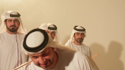 Specific signals and movements for folk dance, a traditional celebration and national occasion, a heritage folklore troupe, dancing with canes and celebrating the national holiday, popular Ayala dances at the festival, a close-up shot of a group of Arab Gulf Emirati men wearing traditional attire dancing a folk dance.
