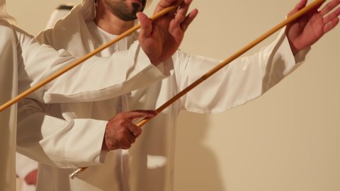 Harmony and coordination in dance movements during a national holiday, Al Ayala is a folk dance at festivals, interaction and dancing with sticks, a traditional celebration and a national occasion, a heritage folklore troupe, celebrating the national holiday, a close-up shot of an Emirati Gulf Arab man wearing traditional attire dancing with a team.