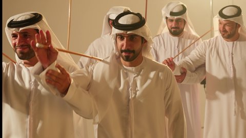 Pride in national identity and heritage, dancing with the khazaan and celebrating the national holiday, festive atmosphere with the traditional Ayala dance, folk dances at the festival, close-up shots of a group of Arab Gulf Emirati men wearing traditional attire dancing a folk dance, heritage folklore performances.