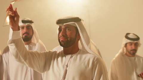 A national occasion and traditional celebration, a folklore heritage troupe, preserving national customs and heritage, dancing with the khazeen and celebrating the national holiday, folk dances at the festival, close-up shots of a group of Arab Gulf Emirati men wearing traditional attire dancing a folk dance.