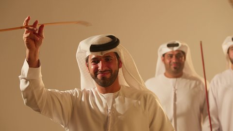 Festive atmosphere, traditional Ayala dance, folklore troupe, preserving national customs and heritage, dancing with canes and celebrating the national holiday, folk dances at the festival, close-up shots of a group of Arab Gulf Emirati men wearing traditional attire dancing a folk dance.