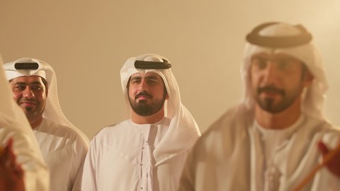 The traditional folklore troupe, preserving national customs and heritage, dancing with the khayzaran and celebrating the national holiday, festive atmosphere, the traditional Ayala dance, folk dances at the festival, close-up shots of a group of Arab Gulf Emirati men wearing traditional attire dancing a folk dance.