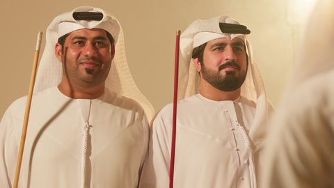 Festive atmosphere, traditional Ayala dance, celebrating the national holiday with cane dancing, folk dances at national events and festivals, close-up shots of a group of Arab Gulf Emirati men wearing traditional attire dancing a folk dance, heritage folklore performances.