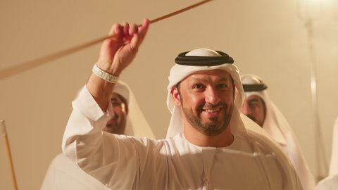 ايماءات السرور والفخرفي عروض الفلكلور التراثي، الاحتفال بالعيد الوطني بالرقص بالخيرزان جزء من الزي التقليدي للامارات، رقصات شعبيه في المناسبات الوطنية والأعياد، تصوير مقرب لمجموعة من الشباب العربين الخليجين الاماراتيين  يرقصون رقصة شعبية اليولة