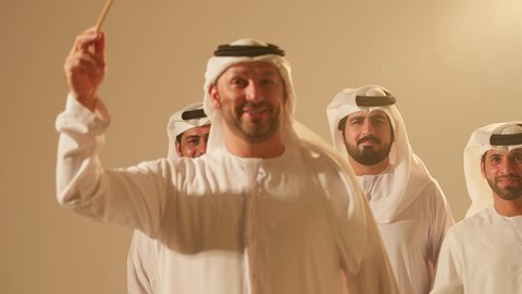 Heritage shows and arts, celebrating the national holiday with the traditional dance using the cane is part of the traditional attire of the Emirates, heritage folklore performances, folk dances during national occasions and holidays, close-up shots of a group of young Arab Gulf Emiratis wearing traditional attire dancing the folk dance Al Ayala.