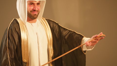 A young man dances using the traditional sticks of Al Ayala, preparing and getting ready to enter the wedding, showing loyalty and love for the homeland. It is a performance art that combines dance, celebrations at Emirati weddings, folk theatrical performances, and folk dances at weddings and events, capturing the wonderful atmosphere of an Emirati Gulf Arab groom.