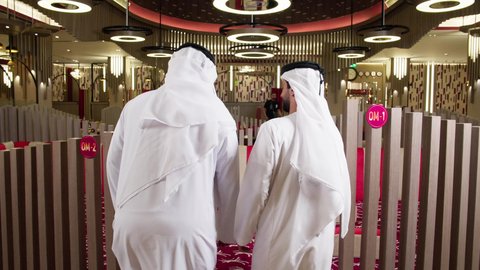 ايماءات تدل على الحركة والمشي, التقدم الى الامام,  قضاء وقت ممتع في الخارج, الترفيه والتسلية في العطلة, تصوير من الخلف لرجلان عربيان خليجيان اماراتيان يرتديان الكندورة و الغتره يسيران داخل المطعم, الاستمتاع بتناول وجبات لذيذة