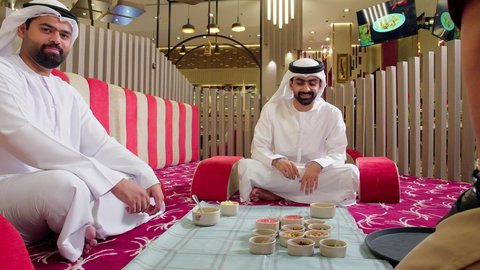 الاجتماع على طاولة الطعام، دعوة الاصدقاء لتناول وجبة شهيه, رجل عربي خليجي اماراتي يرتدي الكندورة و الغتره يجلس برفقة صديقة على المائده، إيماءات السعادة و السرور بقضاء وقت ممتع مع الأصدقاء, ، أكلة شعبية خليجية اماراتية