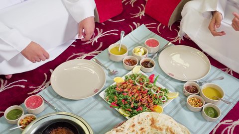 فطور صحي لذيذ, تصوير مقرب لرجل عربي خليجي اماراتي يرتدي الكندورة يقوم بتقديم  اطباق من الطعام الشعبي الاماراتي ، وصفات طعام تقليديه على المائدة  في الامارات