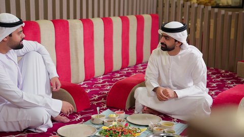 سفرة طعام بأصناف متنوعة, الدردشة والتسامر وقضاء وقت ممتع ,لمة الاصدقاء على سفرة الطعام ,  جلسة وناسة في عطلة نهاية الاسبوع, صديقان عربيان خليجيان اماراتيان يرتديان الكندورة والغتره يجلسان فى مطعم ,