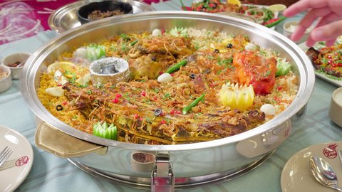 A table filled with a variety of delicious Eastern dishes, popular Arab Gulf Emirati meals, tasty food, a close-up shot of the hand of an Arab Gulf Emirati man eating fresh meat in a restaurant.