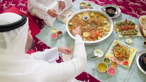 A table filled with a variety of delicious Eastern dishes, having lunch at the restaurant, restaurants and cafes in the UAE, a close-up shot of two Emirati Gulf Arab men wearing the kandura and ghutrah sitting at the table enjoying their meal, spending enjoyable times outdoors.