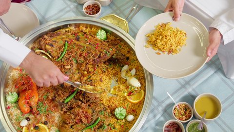 تقديم الطعام في الأطباق وتوزيعه, قضاء أوقات ممتعة, طبق أرز شعبي مع اللحم المبهر مجهز في المطبخ الاماراتي , وصفات الأكلات الشعبية, تصوير مقرب  لرجل عربي خليجي اماراتي يرتدي الكندورة يجلس على سفرة الطعام  يقوم بتحضير طبق الطعام
