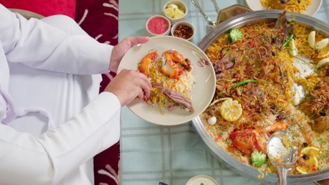 طبق أرز شعبي مع اللحم المبهر مجهز في المطبخ الاماراتي , وصفات الأكلات الشعبية, تصوير مقرب  لرجل عربي خليجي اماراتي يرتدي الكندورة و الغتره يجلس على سفرة الطعام في المطعم يقوم بتناول وجبة الغداء