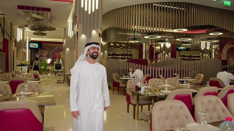 Greeting and peace, the concept of reception and welcome, a session of youth entertainment and amusement, friendship and acquaintance and building relationships, two young Arab Gulf Emiratis wearing kandura and ghutrah sitting at a fine restaurant at a table, enjoying a good time outdoors.