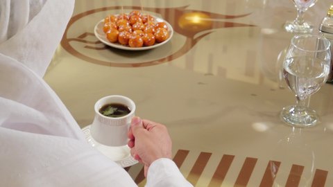 تعديل المزاج بشرب الكافيين, الاستمتاع باحتساء المشروب المفضل،تصوير مقرب من الخلف لرجل عربي خليجي اماراتي يرتدي الكندورة و الغتره يجلس داخل المطعم يمسك بيديه كوب من القهوة , قضاء وقت ممتع فى الخارج