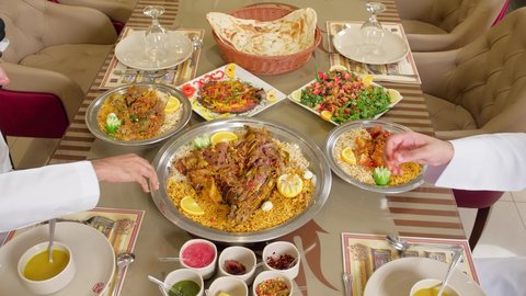 مطاعم و كافيهات في الإمارات ، تناول الغداء في المطعم, تصوير مقرب لرجلان عربيان خليجيان اماراتيان يرتديان الكندورة و الغتره يجلسان على المائدة يقومان بتناول الطعام ، قضاء الأوقات الممتعة في الخارج، سفرة مليئة باصناف من المأكولات الشرقية الشهية