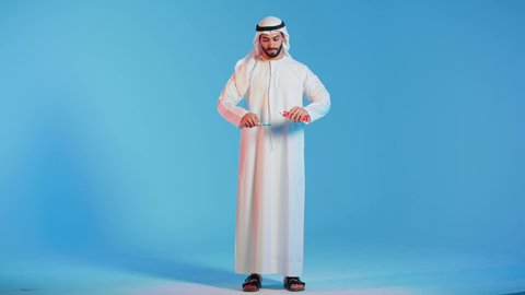 بورتريه لرجل عربي خليجي اماراتي يرتدي الكندورة والغترة البيضاء  يقوم بتنظيف الأسنان بفرشاة الأسنان ،تجنب تسوس الاسنان وامراض اللثة ،  مفهوم العناية والإهتمام بصحة ونظافة الأسنان ، روتين نظافة الفم اليومية ، خلفية ملونة