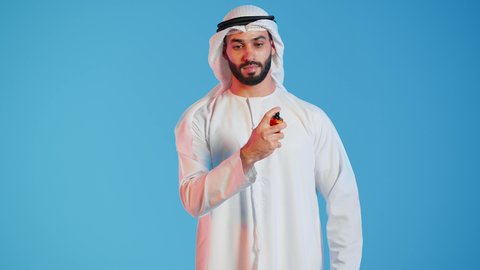 عطور ذات روائح فاخرة وفريدة، مناسبات الأعياد وحفلات الزفاف، التسويق لمنتجات العطور، العود العطري، بورتريه لرجل عربي خليجي اماراتي يرتدي الكندورة والغترة البيضاء  يقوم بوضع العطر، التطيب والتعطر، مفهوم الأناقة والإهتمام المظهر الخارجي، خلفيه ملونه