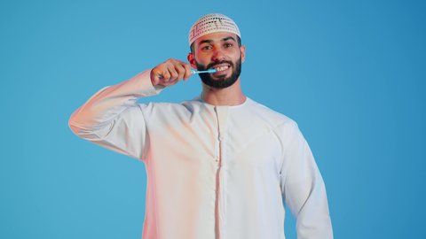 عادات صحية ونظافة شخصية, بورتريه لرجل عربي خليجي اماراتي  يقوم بتنظيف الأسنان بفرشاة الأسنان ، مفهوم العناية والإهتمام بصحة ونظافة الأسنان ، روتين نظافة الفم اليومية ، تجنب تسوس الاسنان وامراض اللثة ، خلفية ملونة