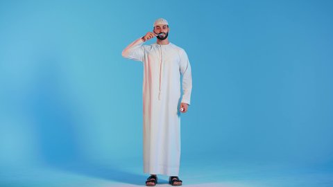 بورتريه لرجل عربي خليجي اماراتي  يقوم بتنظيف الأسنان بفرشاة الأسنان ، مفهوم العناية والإهتمام بصحة ونظافة الأسنان ، روتين نظافة الفم اليومية ، تجنب تسوس الاسنان وامراض اللثة ، خلفية ملونة