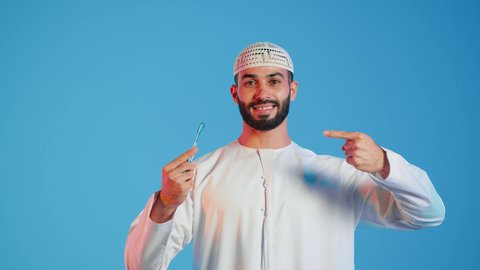 الإهتمام المظهر الخارجي ،  مفهوم العناية بالبشرة والنظافة ، شفرة حلاقة رجالية، بورتريه لرجل عربي خليجي اماراتي يرتدي الزي الاماراتي يشير بيده الي شفرة الحلاقة  ،خلفية ملونة