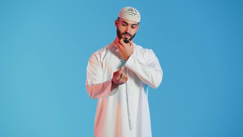 مفهوم العناية بالبشرة والنظافة ،بورتريه لرجل عربي خليجي اماراتي يرتدي الزي الامارات  يمسك بيده شفرة الحلاقة بايماءات التفكير والحيرة ،  الإهتمام المظهر الخارجي ، شفرة حلاقة رجالية، خلفية ملونة